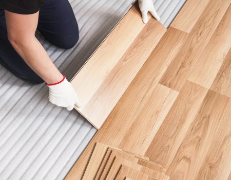 Installing laminated floor, detail on man hands holding wooden tile, over white foam base layer