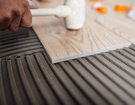 Flooring and tiling. Professional tiler placing floor tiles on adhesive surface.