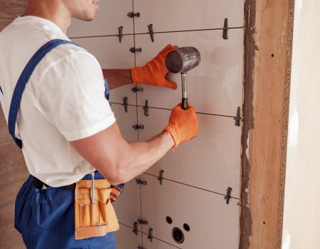 Close up of young man construction worker using rubber hammer while placing tile on the wall